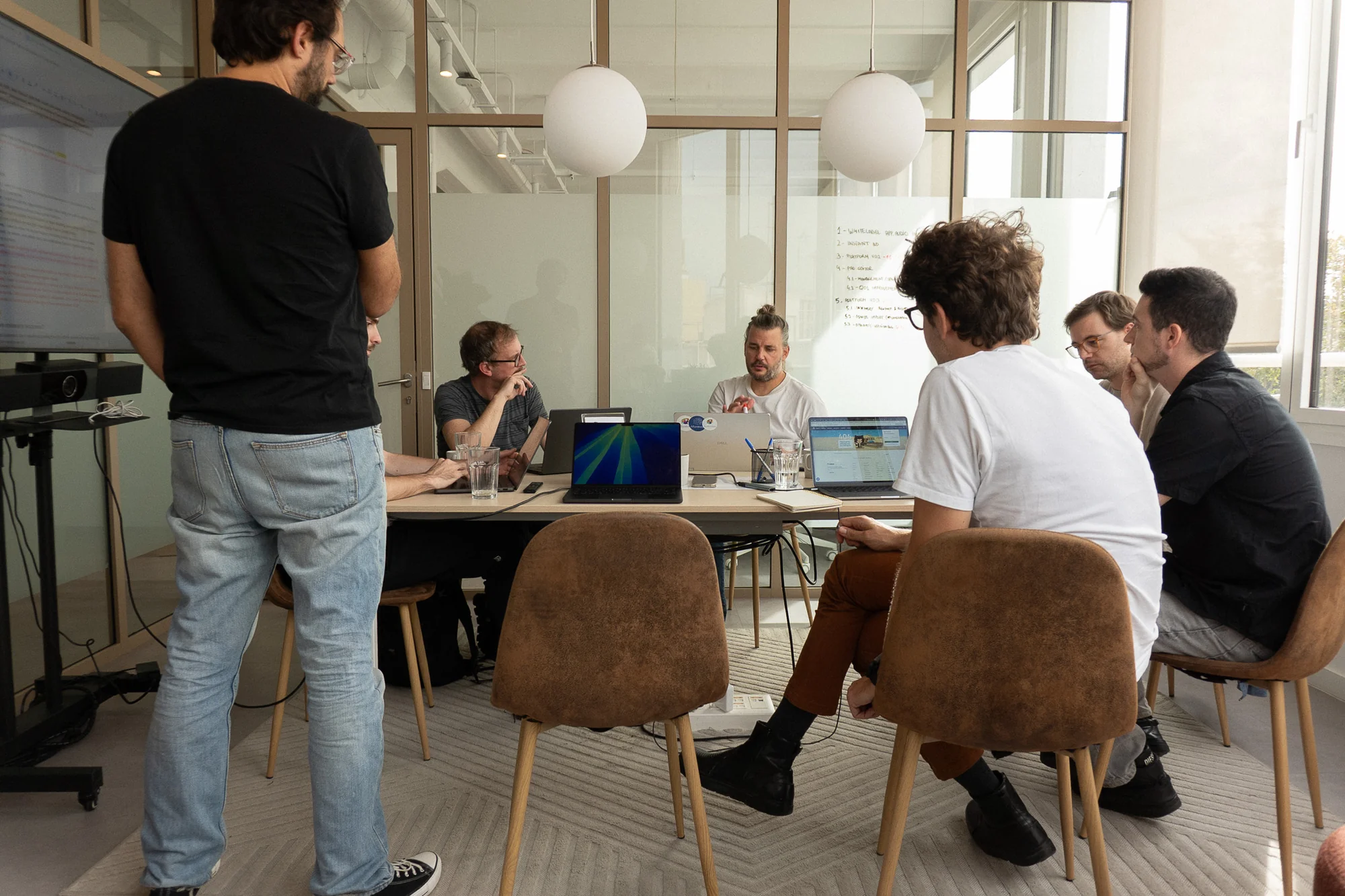 A team around a meeting table of laptops, a numbered plan written on the glass wall behind them.