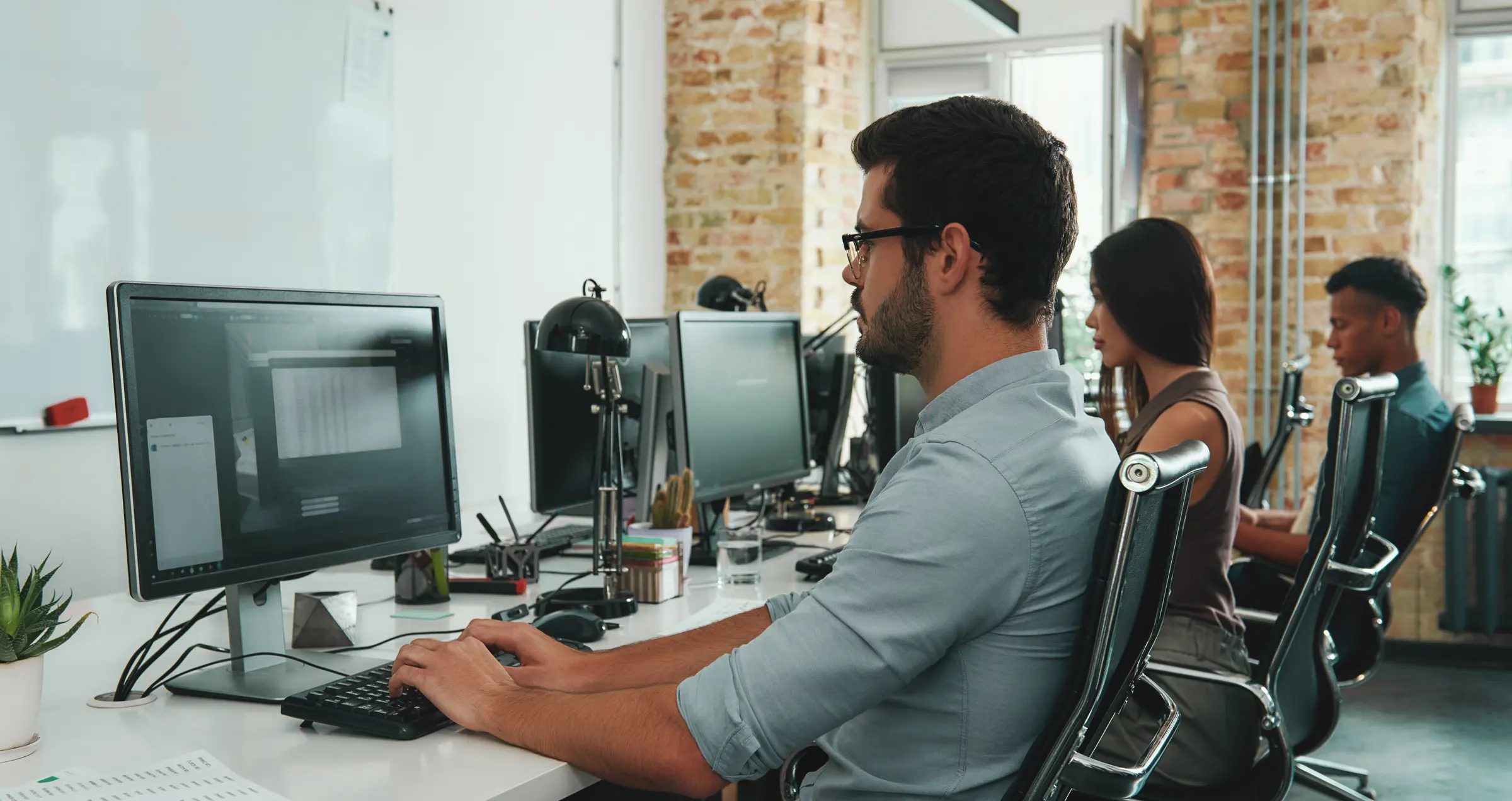 An engineer at his desk in an open-plan office, colleagues working down the row.